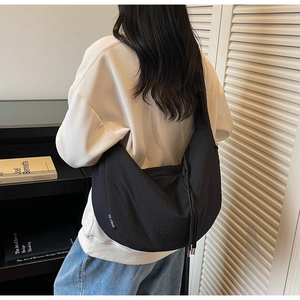 Close-up of black nylon crescent crossbody bag with branded label on a casual model