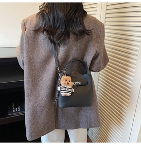 Detail of black pebbled leather bucket bag with silver twist lock and cute bear charm