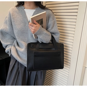 Minimalist black leather tote bag with large front pocket and top handles for commuting