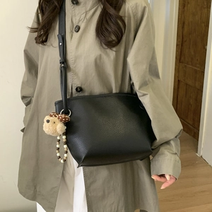 Close-up of black lychee grain leather crossbody bag with cute plush puppy charm