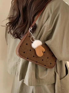 Brown polka dot underarm bag with plush glove charm shown on model in olive green outfit