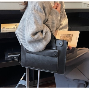 Dettaglio della borsa in pelle nera con tasca frontale e borchie metalliche sul modello