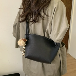 Detail of black pebbled leather bucket bag with cute dog charm on casual trench coat