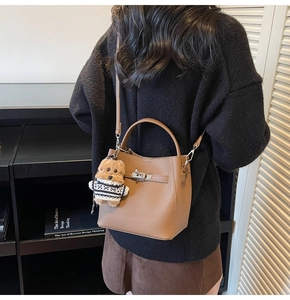 Detail of a brown lychee pattern bucket bag with silver lock and a cute bear charm