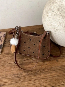 Brown polka dot shoulder bag with bow and plush pompom charm on a wooden background