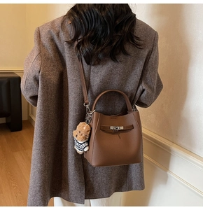 Detail of dark brown leather bucket bag with metal lock and cute bear charm pendant