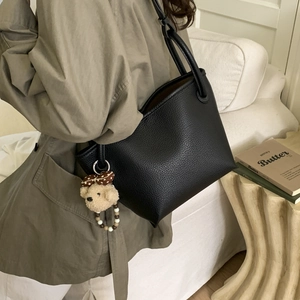 Detail of black pebbled leather tote bag with a cute plush bear charm on a cream sofa