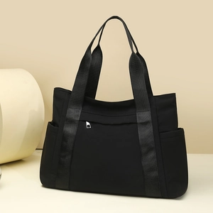 Detail view of large black nylon tote bag showing metal zipper and side pocket features