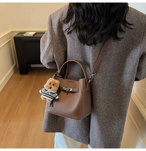 Detail of dark brown leather bucket bag with silver twist lock and cute bear charm