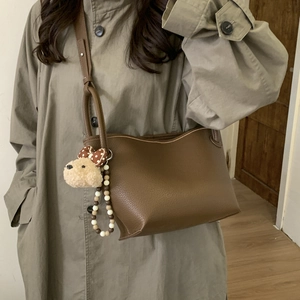 Crossbody view of brown lychee grain leather bucket bag with cute plush puppy charm detail