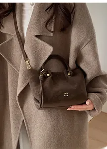 Detail of dark brown leather bucket bag with gold lettering and tassel on wool coat