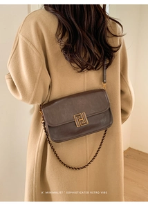 Détail du sac bandoulière marron foncé avec boucle dorée et chaîne sur un manteau en laine