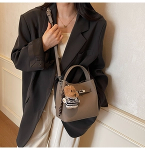 Detail of dark khaki lychee leather bucket bag with silver turn-lock and bear charm
