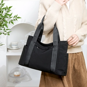 Detail of a black nylon tote bag featuring front zip pocket and side compartments for storage