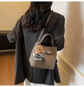 Detail of grey lychee leather bucket bag with dog plush pendant shown from a back view