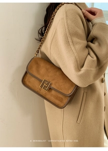 Détail du sac bandoulière en daim marron avec fermoir doré sur manteau beige