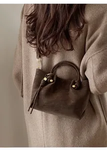 Detail of a dark brown suede bucket bag featuring golden logo and soft pleated leather