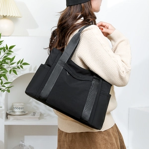 Detail of black nylon tote bag featuring side pockets and reinforced gray webbing handles