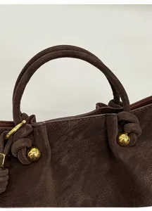 Detail of dark brown leather handbag featuring unique knot design and gold metal hardware
