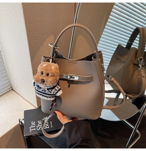 Detail of grey lychee leather bucket bag with silver lock and plush dog charm