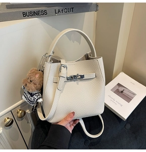 Detail of cream pebbled leather bucket bag with metal clasp and cute bear charm