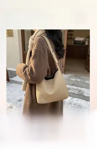 Close-up of beige lychee pattern leather tote bag with silver hardware on snowy background