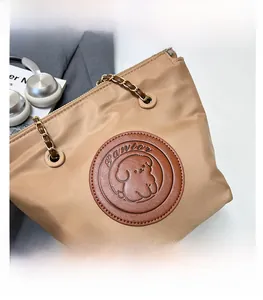 Détail du sac seau en nylon kaki avec écusson en cuir teddy et bandoulière en chaîne