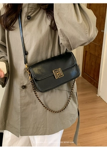 Sac à bandoulière rétro en cuir noir avec fermoir doré porté sur un trench-coat classique