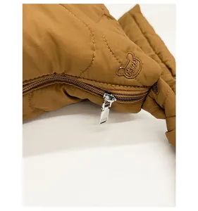 Détail macro du sac en nylon marron matelassé avec broderie ours et fermeture éclair argentée