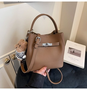 Detail of brown litchi leather bucket bag featuring silver lock and cute bear charm
