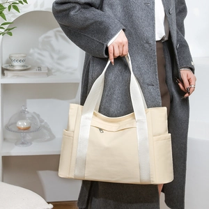 Nylon tote bag with wide webbing handles and side pockets shown in a minimalist room