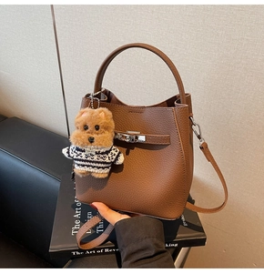 Detail of dark brown pebbled leather bucket bag with silver buckle and plush puppy charm
