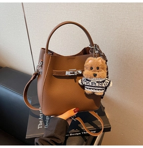 Detail of brown leather bucket bag with silver metal turn-lock and plush doll pendant