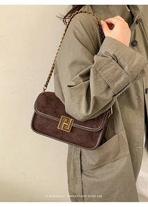 Détail du sac bandoulière en daim marron avec boucle dorée et chaîne sur un mannequin