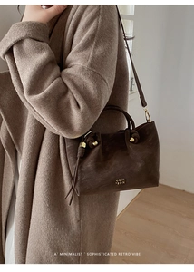Detail of dark brown leather bucket bag with gold logo and knotted handle decor