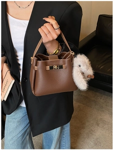 Detail of dark brown litchi pattern leather bucket bag with plush charm and gold clasp