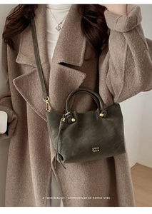 Detail of dark olive green bucket bag with drawstring closure and golden ball ornament