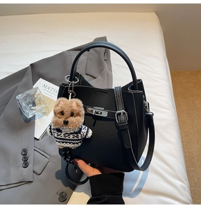 Close-up of black lychee texture leather bucket bag with silver clasp and plush dog charm