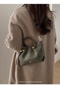 Detail of dark green bucket bag with gold metal logo and decorative beaded handle