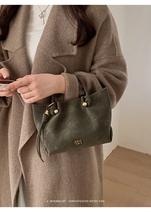 Detail of minimalist green bucket bag with knotted handle and gold sphere buckle detail