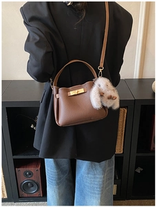 Detail of brown pebbled leather bucket bag featuring a gold lock and plush bunny charm