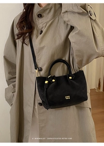 Detail of a black suede crossbody bucket bag featuring gold hardware and logo branding