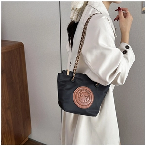 Detail of black nylon bucket bag featuring a brown puppy patch and metal chain strap