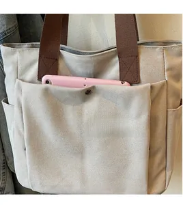 Détail du sac cabas beige montrant une poche avant boutonnée avec une tablette rose