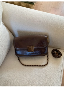 Détail d'un sac à bandoulière en cuir marron rétro avec boucle dorée sur un canapé blanc
