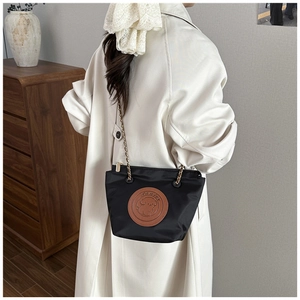 Detail of black nylon bucket bag with gold chain strap and brown puppy leather patch