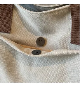 Détail du fermoir magnétique en bronze sur le sac cabas en toile beige à anses marron