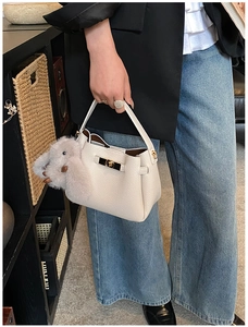 Detail of off-white lychee texture bucket bag with plush rabbit charm and gold hardware