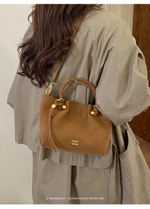 Close-up of brown minimalist leather bucket bag with decorative knot handle and metal rings