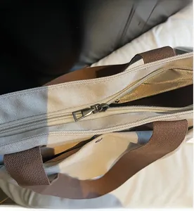 Detail view of smooth metal zipper closure on the off-white canvas tote bag